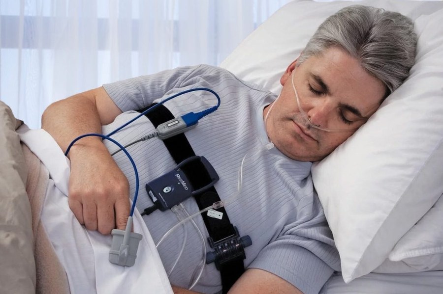 A man asleep in bed wearing the sensors and leads of a home sleep study device